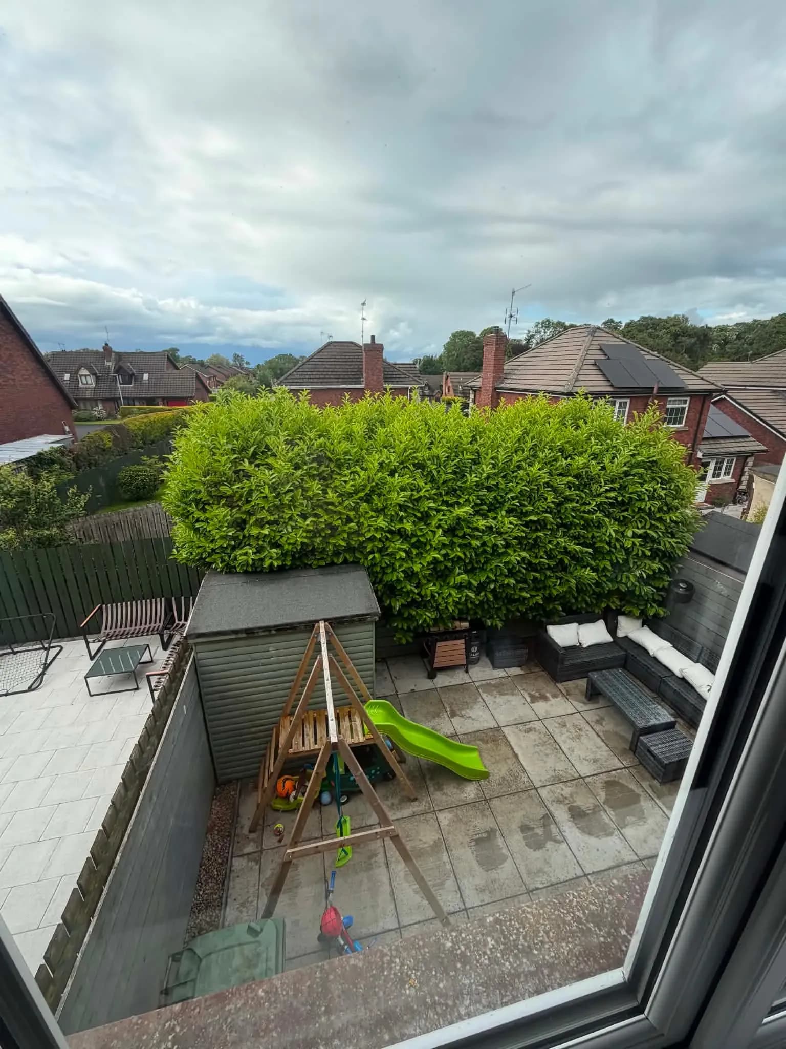 Overgrown laurel hedge towering over a family patio and blocking the light, seen from an upstairs window